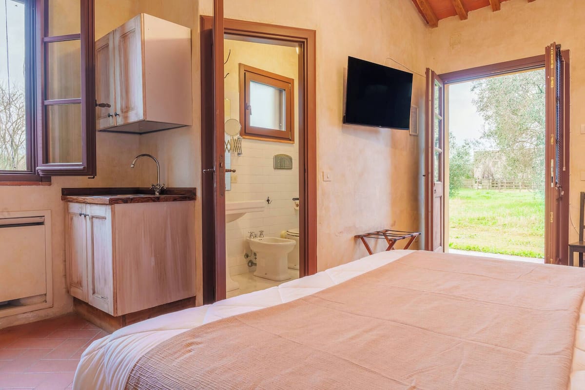 A bedroom with a bed, a bathroom with a sink and toilet, a wooden cabinet, and a TV mounted on the wall.