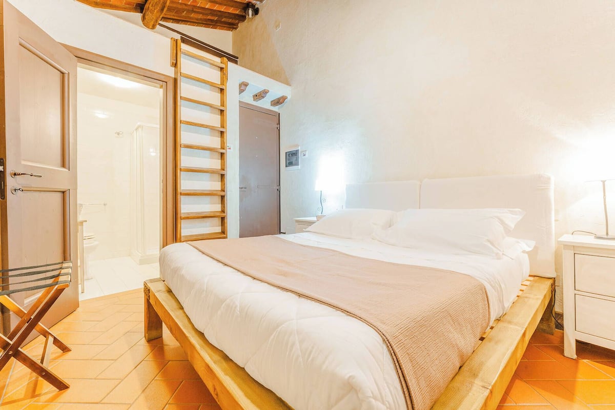 A bedroom with a bed, a wooden ladder, a door, and a nightstand.