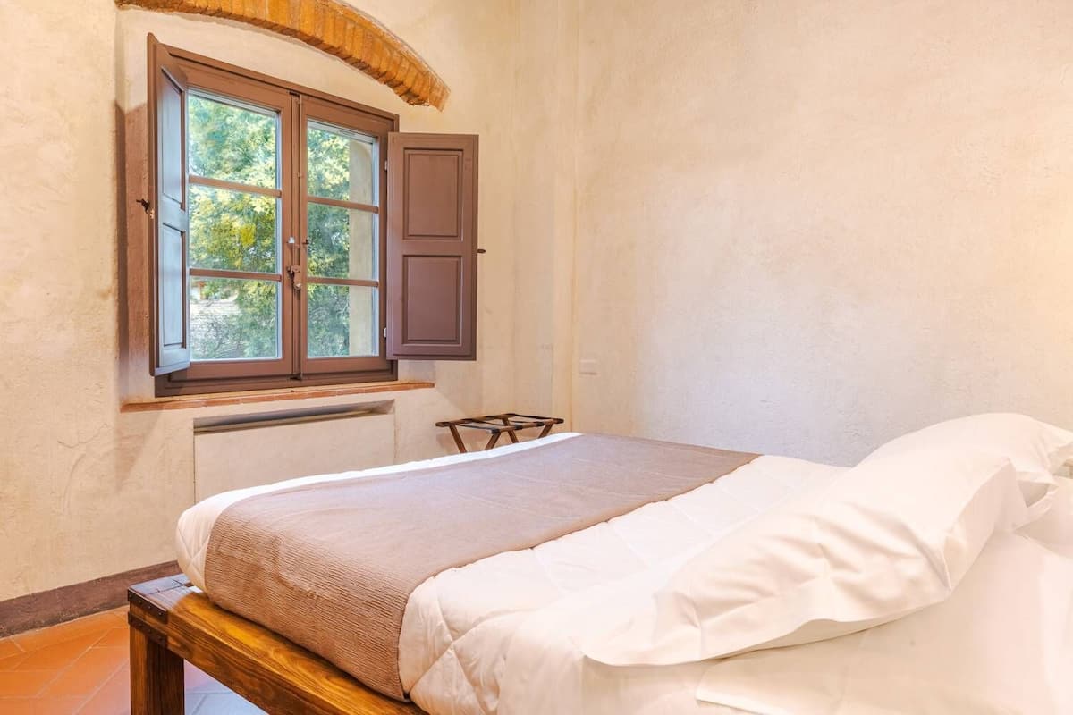 A bedroom with a bed, a window with a wooden shutter, and a small table.
