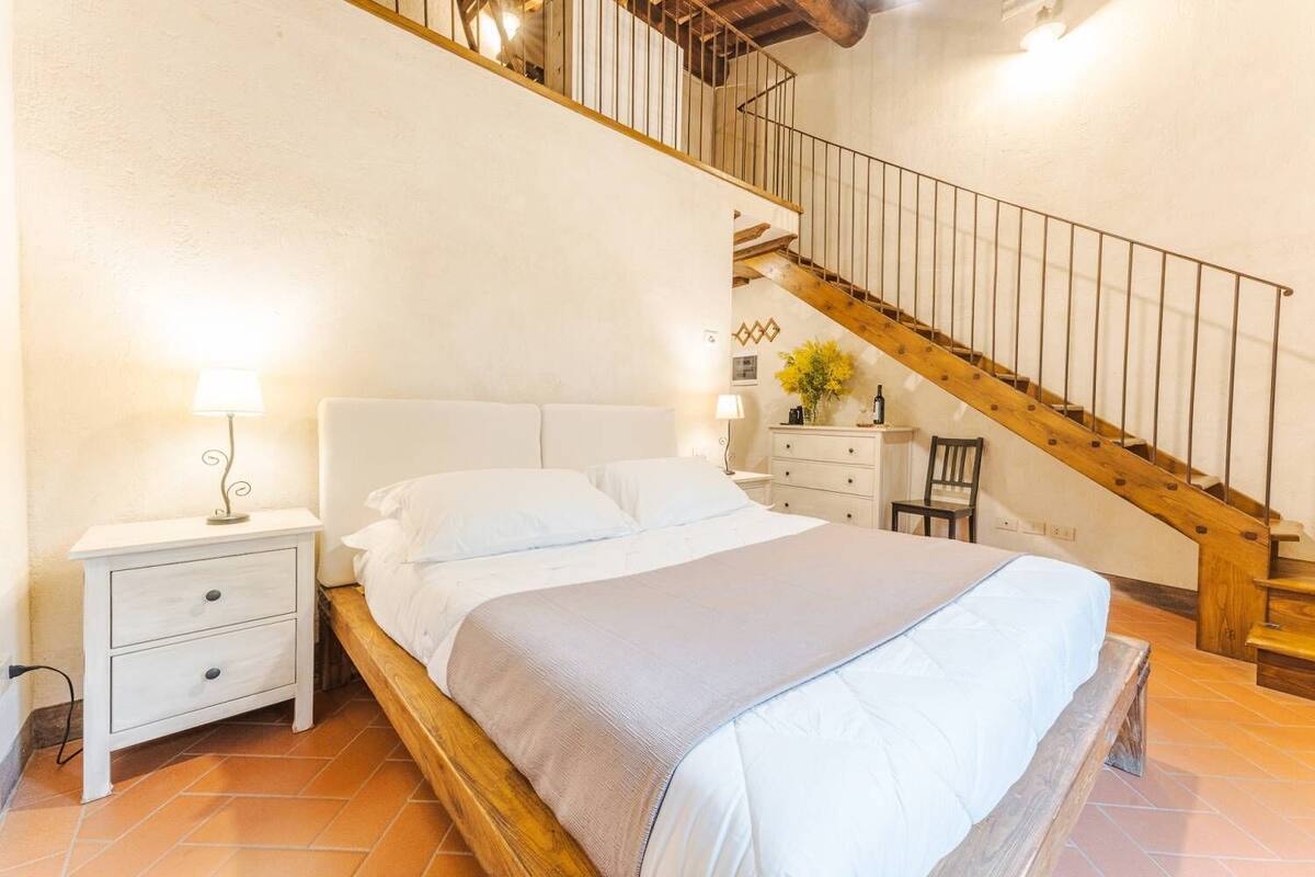 A bedroom with a wooden bed, white nightstands, a dresser, and a wooden staircase.