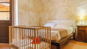 Une chambre avec un berceau, un lit avec du linge de lit blanc, une table de chevet en bois et une lampe.