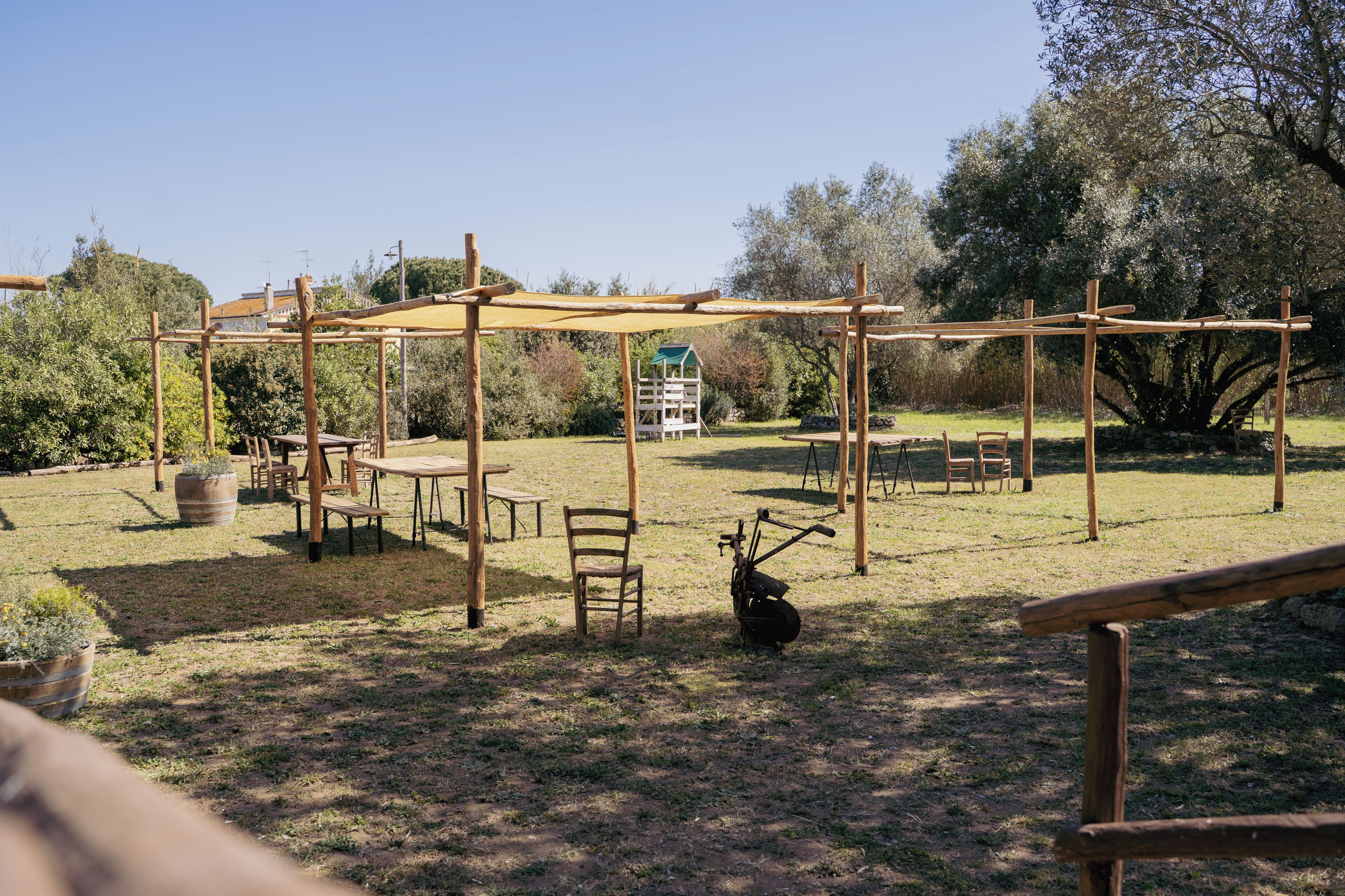 Un espacio al aire libre con mesas y sillas de madera, una estructura de pérgola y un comedero para pájaros.