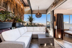 Un balcón moderno con un sofá seccional blanco, una mesa de centro de mimbre y plantas en macetas.