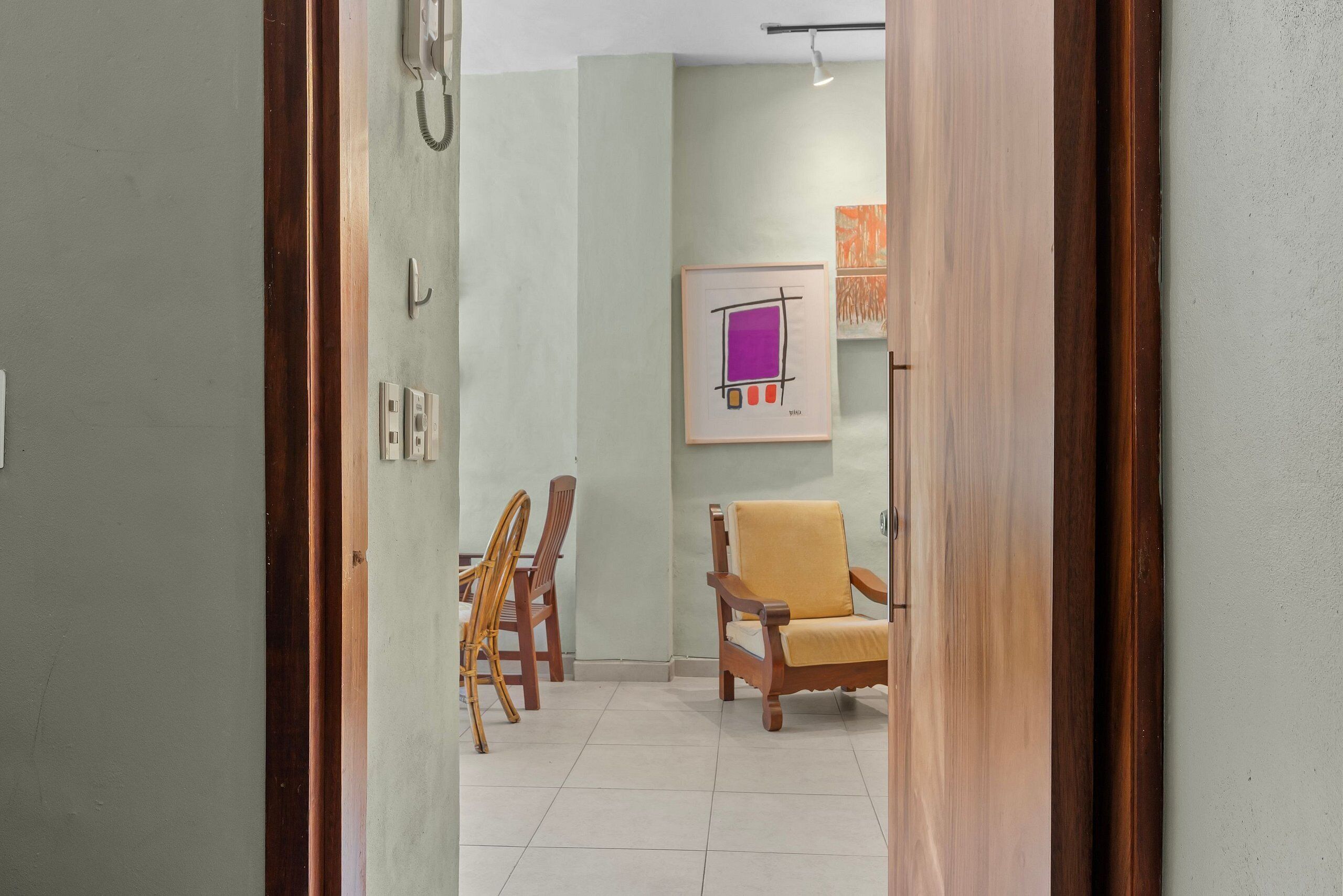 Un pasillo con una silla de madera, un cuadro en la pared y un teléfono.
