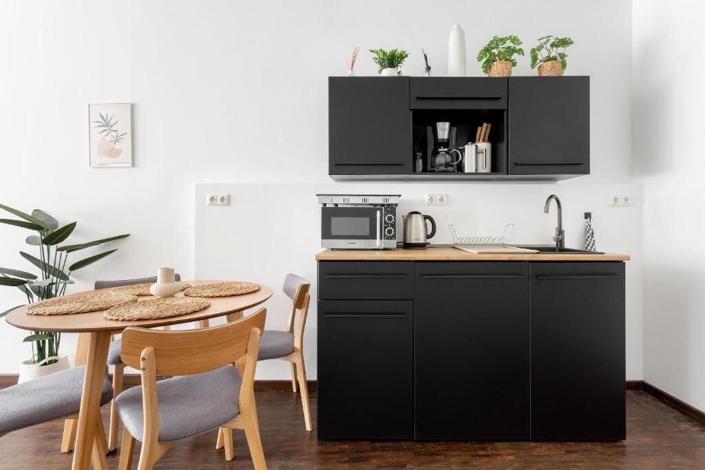 Een compacte keuken met een magnetron, koffiezetapparaat en spoelbak. Twee stoelen en een ronde tafel met geweven placematen.