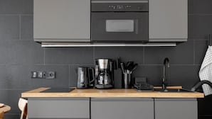 A modern kitchen with grey cabinets, a wooden countertop, a coffee maker, and a sink. - Global Living Augsburg Rathausplatz (Augsburg)