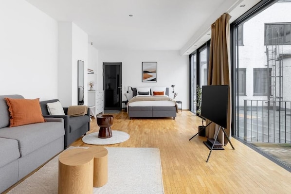 A modern bedroom with a bed, a gray sofa, a coffee table, and a TV.