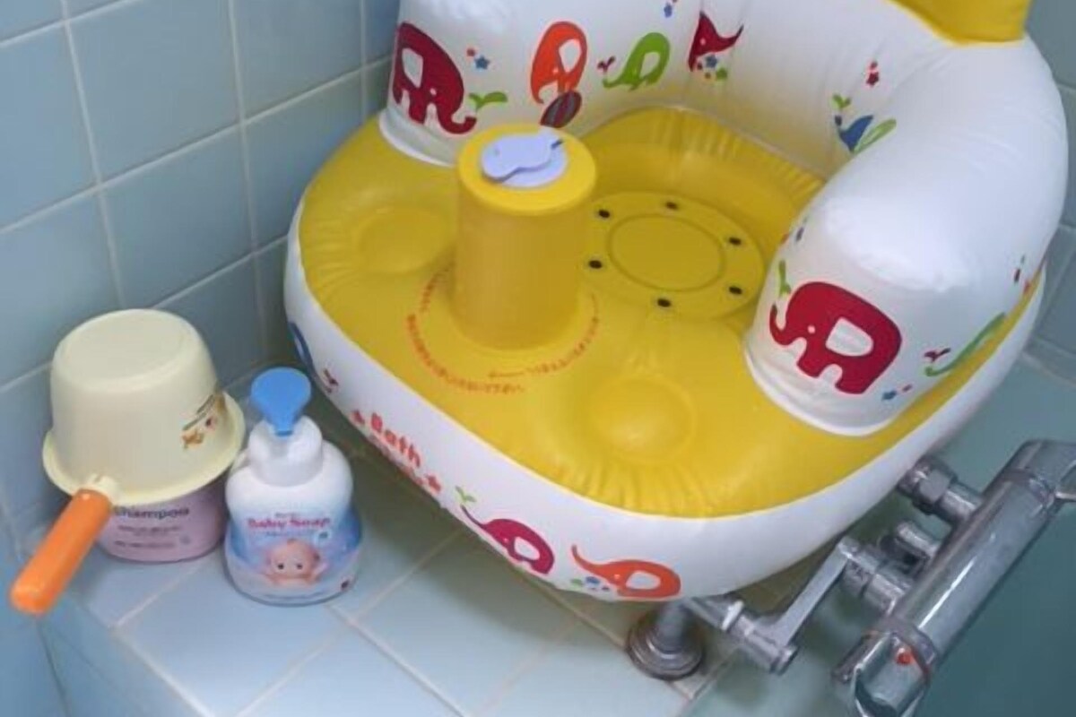 A bathroom with a yellow and white inflatable bath seat, a white basin, a yellow cup, and a bottle of baby shampoo.