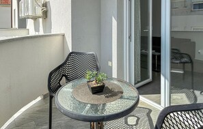 Een glazen tafel met een bloempot, twee stoelen en een schuifdeur die leidt naar een binnenruimte.