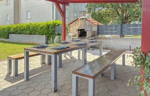 An outdoor patio with a stone barbecue grill, a wooden table set with plates, and benches. - 2 bedroom nice apartment in Cizici (Cizici)