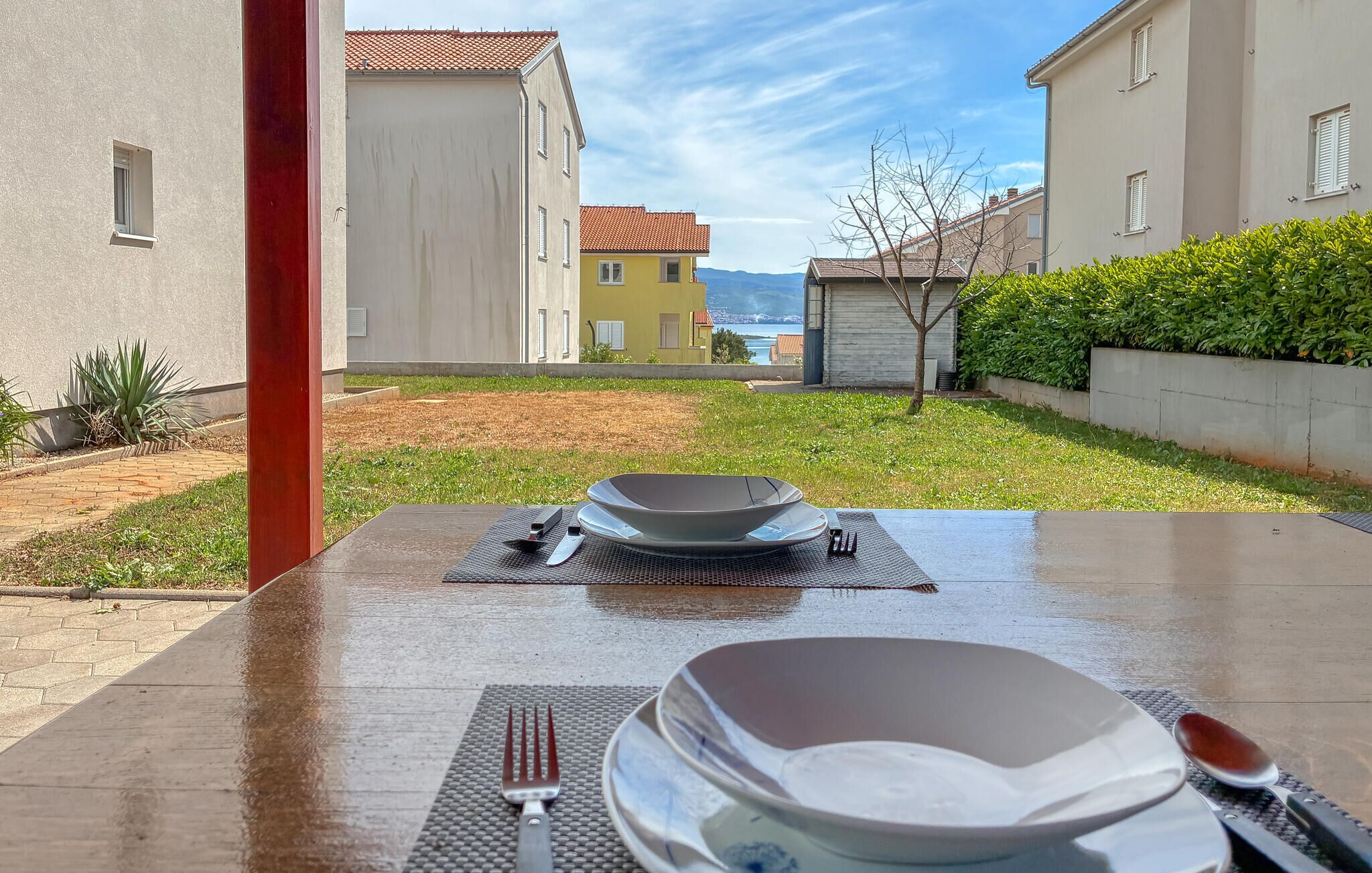 Ein Tisch mit Tellern, Besteck und einer Schüssel in einem Innenhof mit Blick auf Gebäude und ein Gewässer.