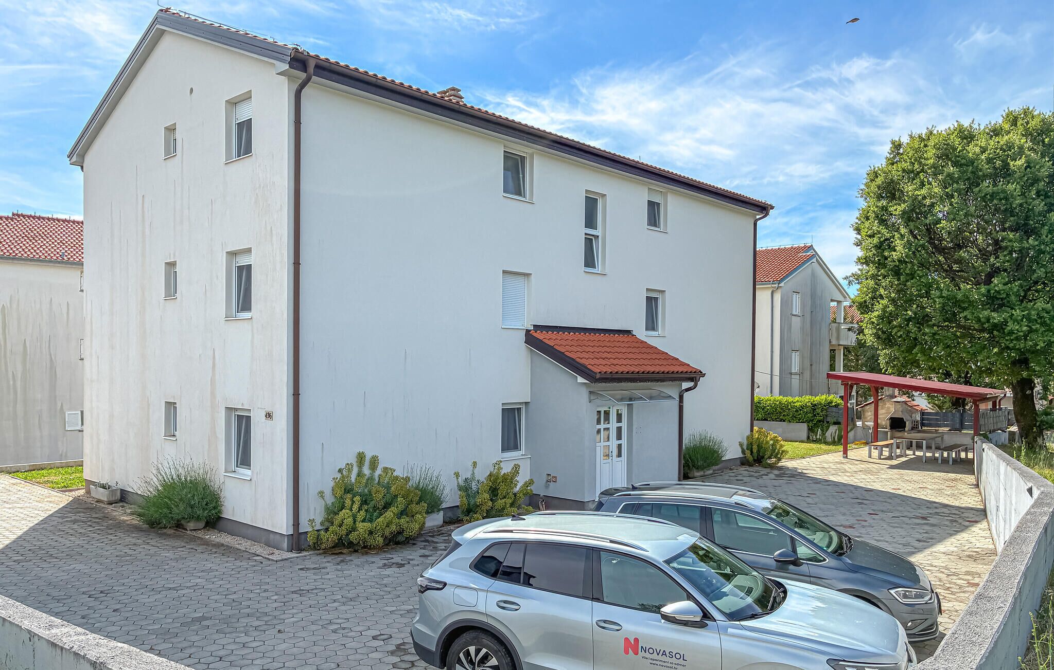 Un bâtiment à deux étages, doté d’un toit recouvert de tuiles rouges, d’une entrée abritée et d’un espace de stationnement pouvant accueillir deux voitures.