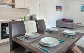Ein Essbereich mit Tisch für vier Personen, eine Küche mit modernen Geräten, ein graues Sofa und Kunstwerke an den Wänden.