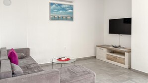 Een woonkamer met een grijze bank, een glazen salontafel, een witte tv-meubel en een flatscreen televisie.
