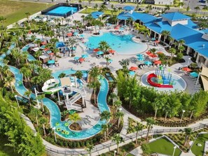 Vista aérea de un resort con varias piscinas, toboganes acuáticos y zonas de descanso rodeado de palmeras.