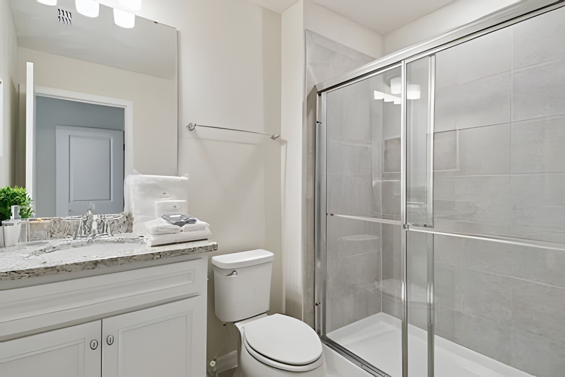 A modern bathroom with a glass shower enclosure, a white toilet, and a marble countertop.