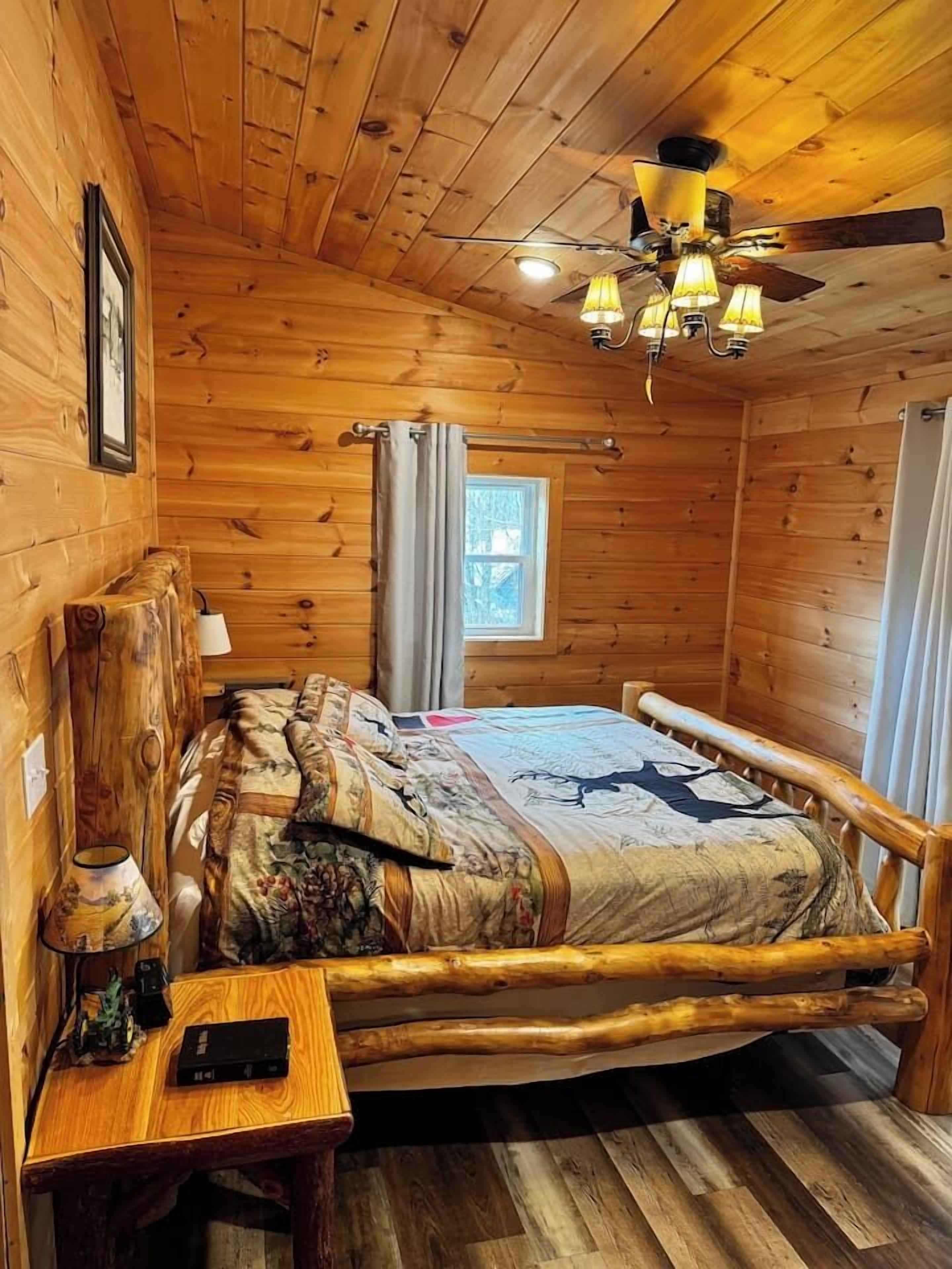 Une chambre dans un chalet en bois, avec un lit, une table de chevet, une lampe et un ventilateur de plafond.
