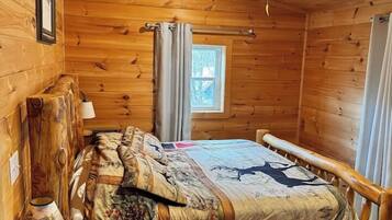 Une chambre dans un chalet en bois, avec un lit, une table de chevet, une lampe et un ventilateur de plafond.
