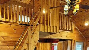 Ein Holzblockhaus-Innenraum mit einer Couch, einer Lampe, einem kleinen Tisch, einer Treppe und einer Küchenzeile.