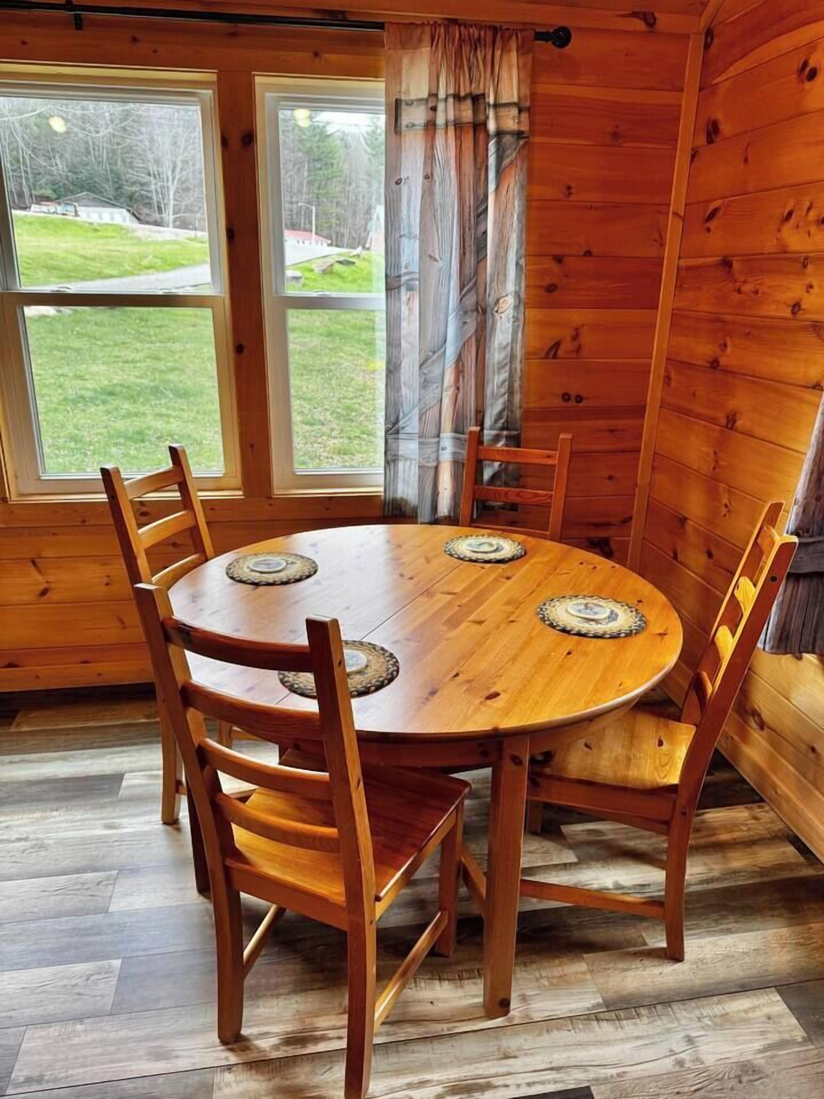 Un intérieur en bois avec une table ronde et des chaises, de grandes fenêtres et une vue sur la verdure environnante.