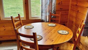 Un intérieur en bois avec une table ronde et des chaises, de grandes fenêtres et une vue sur la verdure environnante.