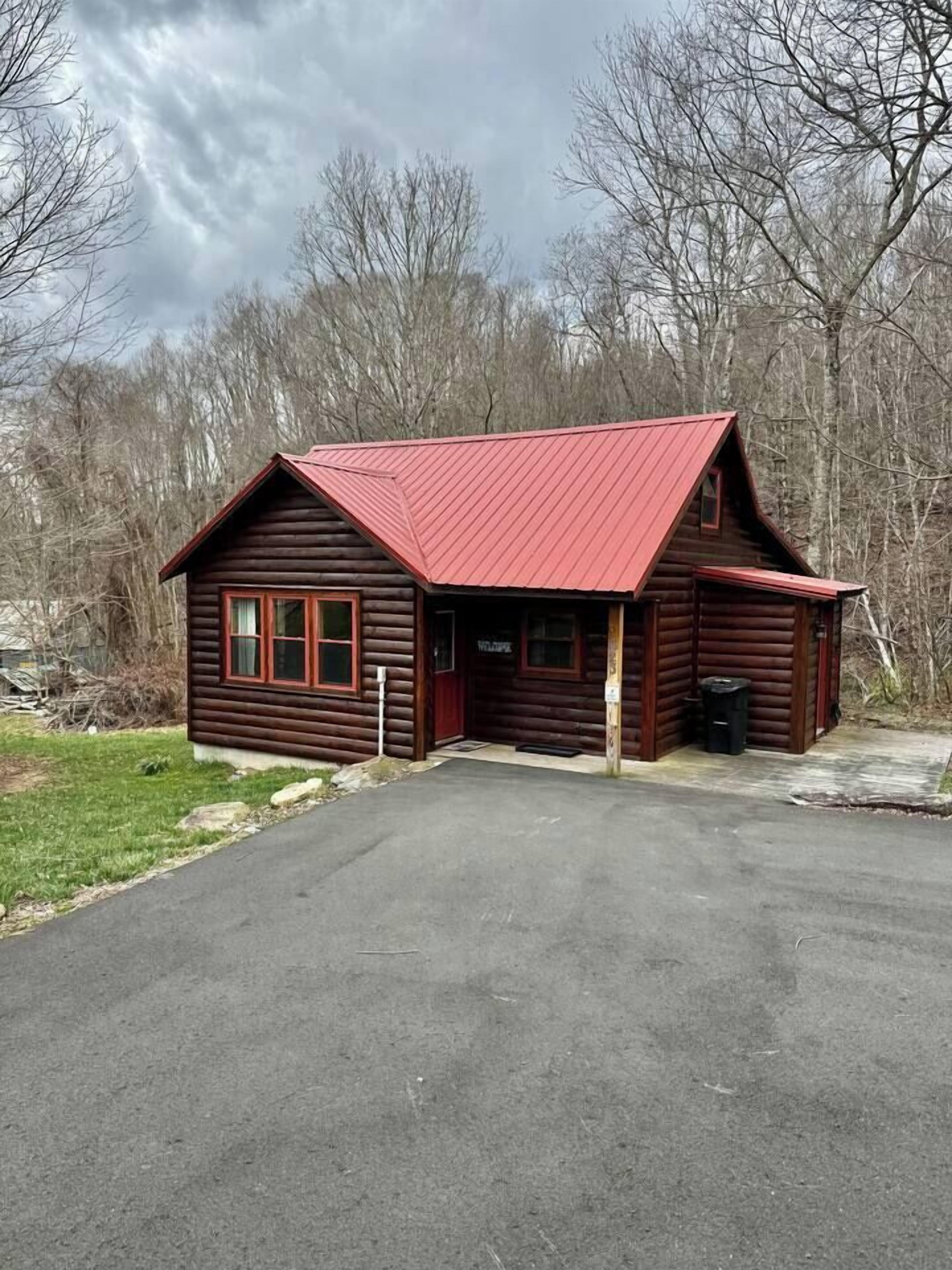 Une cabane en rondins avec un toit rouge, un porche et une pancarte indiquant « Bienvenue ».