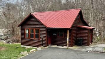 Une cabane en rondins avec un toit rouge, un porche et une pancarte indiquant « Bienvenue ».