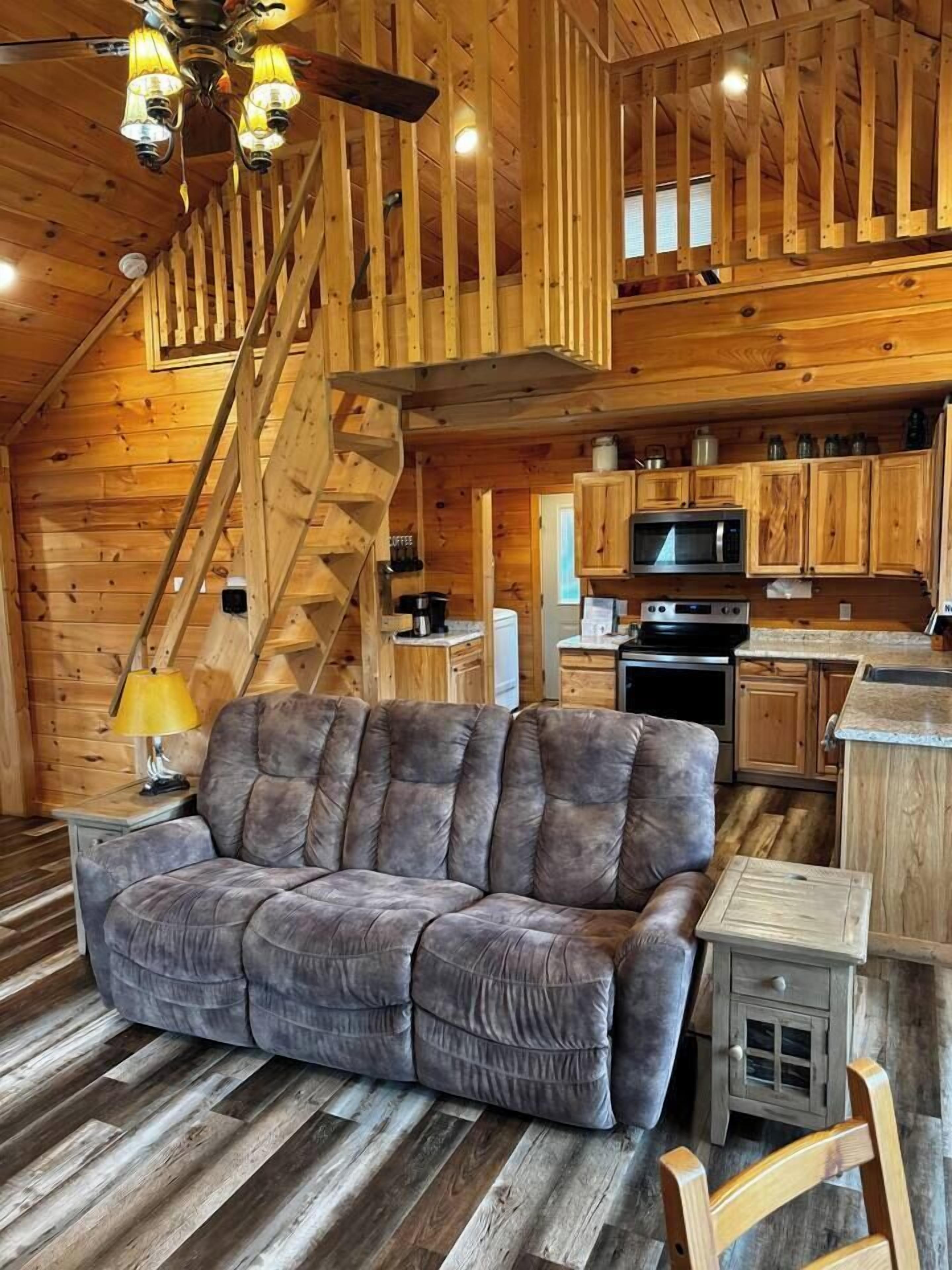 A wooden interior with a sofa, kitchen area, and a staircase.