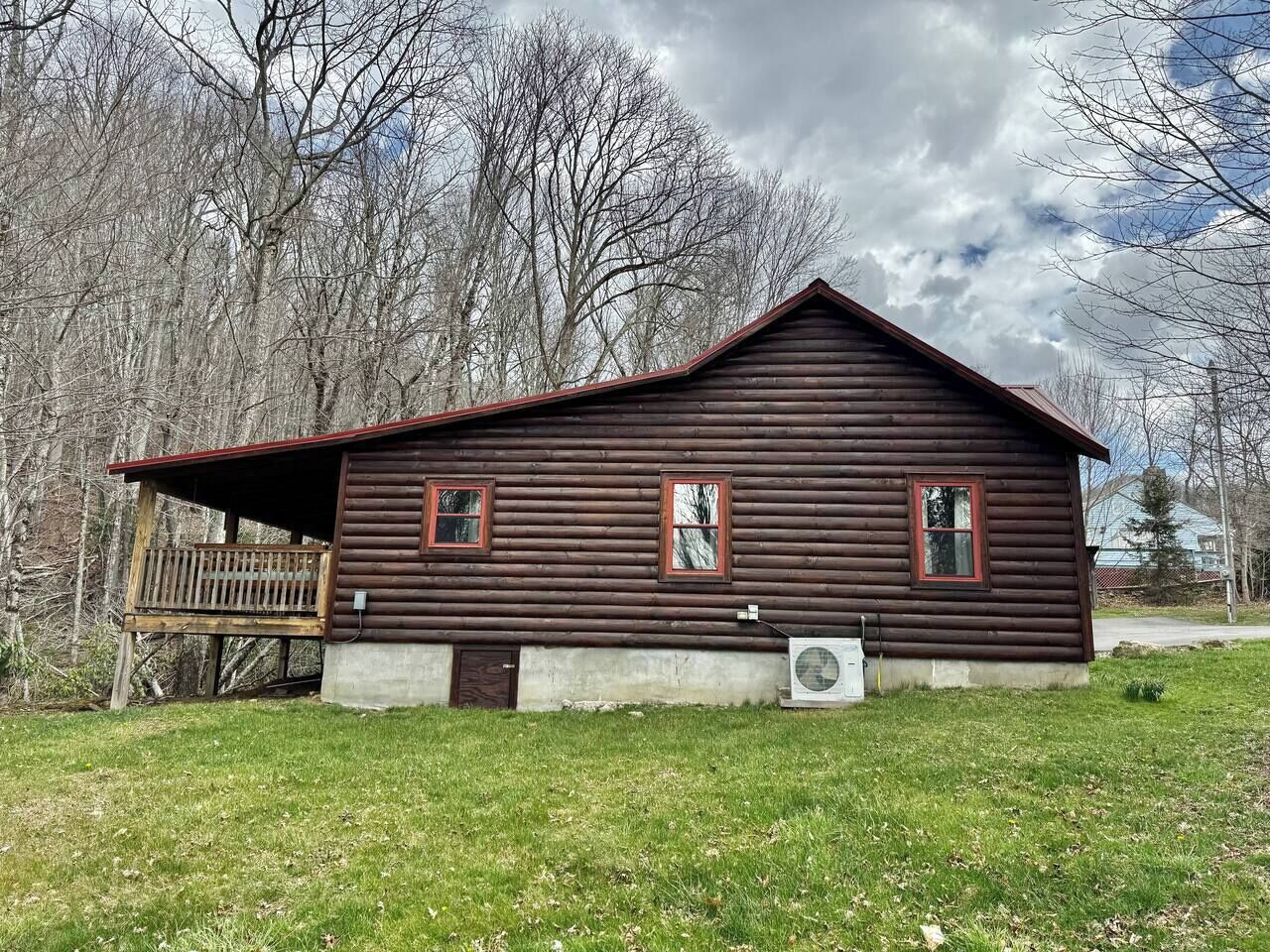 Une cabane en bois avec une véranda, un petit abri attenant et une cour gazonnée.