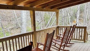 Eine Holzdielen-Terrasse mit Schaukelstühlen, einem Hollerleger und Blick auf Bäume.