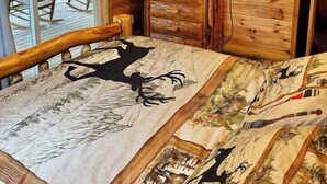 Ein Holzhütten-Innenraum mit einem Bett, einem Fernseher auf einem Holzständer und einem Deckenventilator.