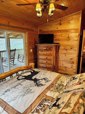 A wooden cabin interior with a bed, a television on a wooden stand, and a ceiling fan. - Creekside Blessings 
Cabin (Beech Mountain)