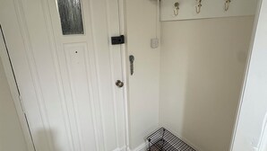 Une porte blanche avec une petite fenêtre, un étagère en métal et un plancher en bois.
