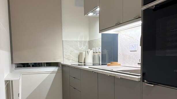 Une cuisine moderne avec des meubles gris, un plan de travail blanc et un four noir.
