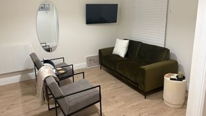 Un salon moderne comprenant un canapé, une table à manger avec des chaises, un téléviseur fixé au mur et un grand miroir.