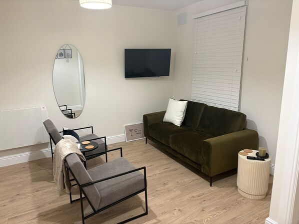 Uma sala de estar moderna com um sofá, uma mesa de jantar com cadeiras, uma TV na parede e um espelho grande.