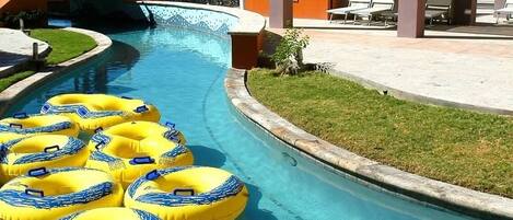 A pool area with yellow and blue inflatable rings, a palm tree, and a covered seating area with a view of the ocean.