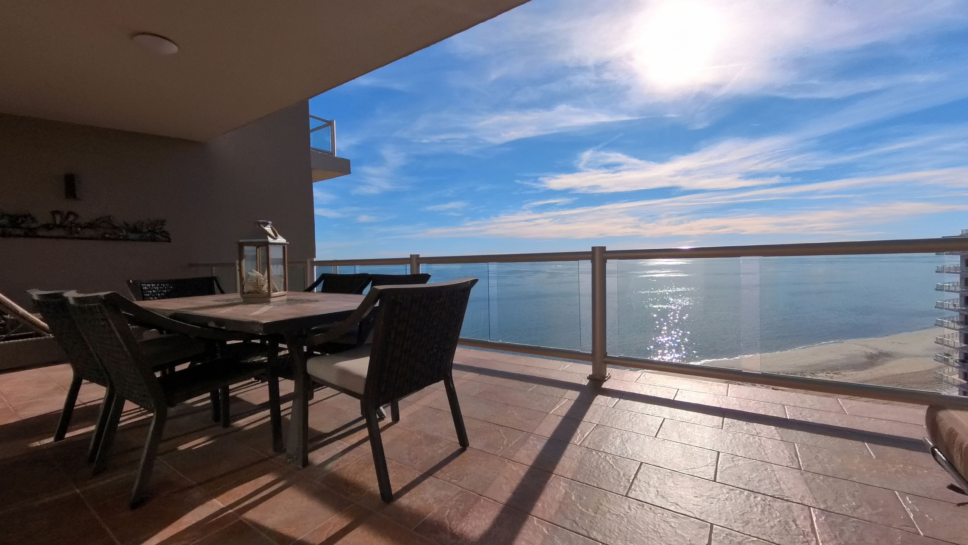 A balcony with a table and chairs, overlooking a body of water and a clear sky.