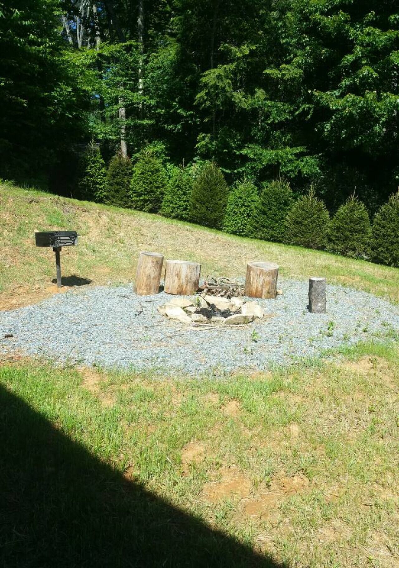 A fire pit area with logs, surrounded by gravel, in a grassy outdoor setting.