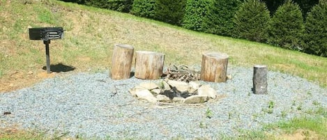 A fire pit area with logs, surrounded by gravel, in a grassy outdoor setting.