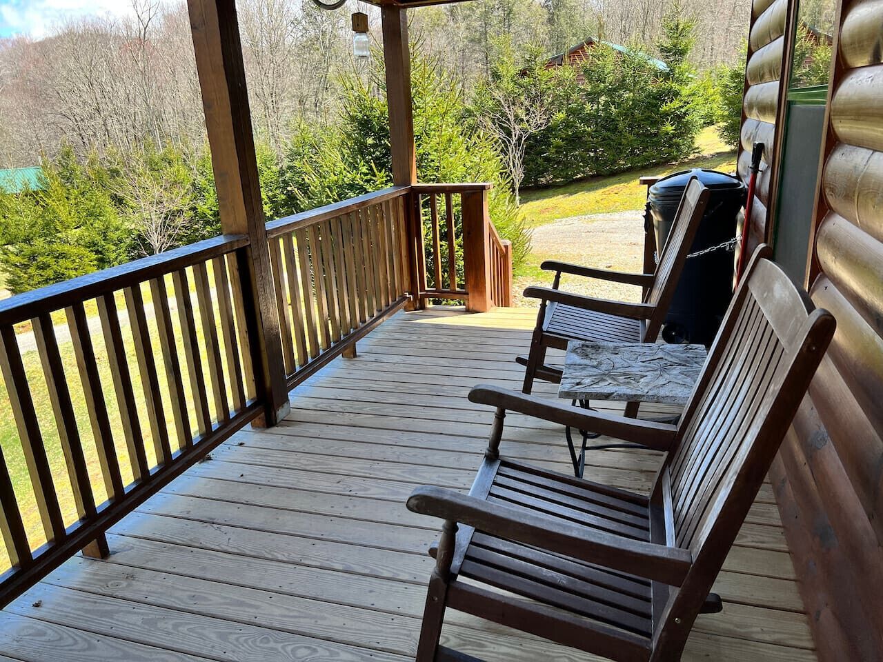 A wooden deck with two wooden chairs and a table, overlooking a forested area.