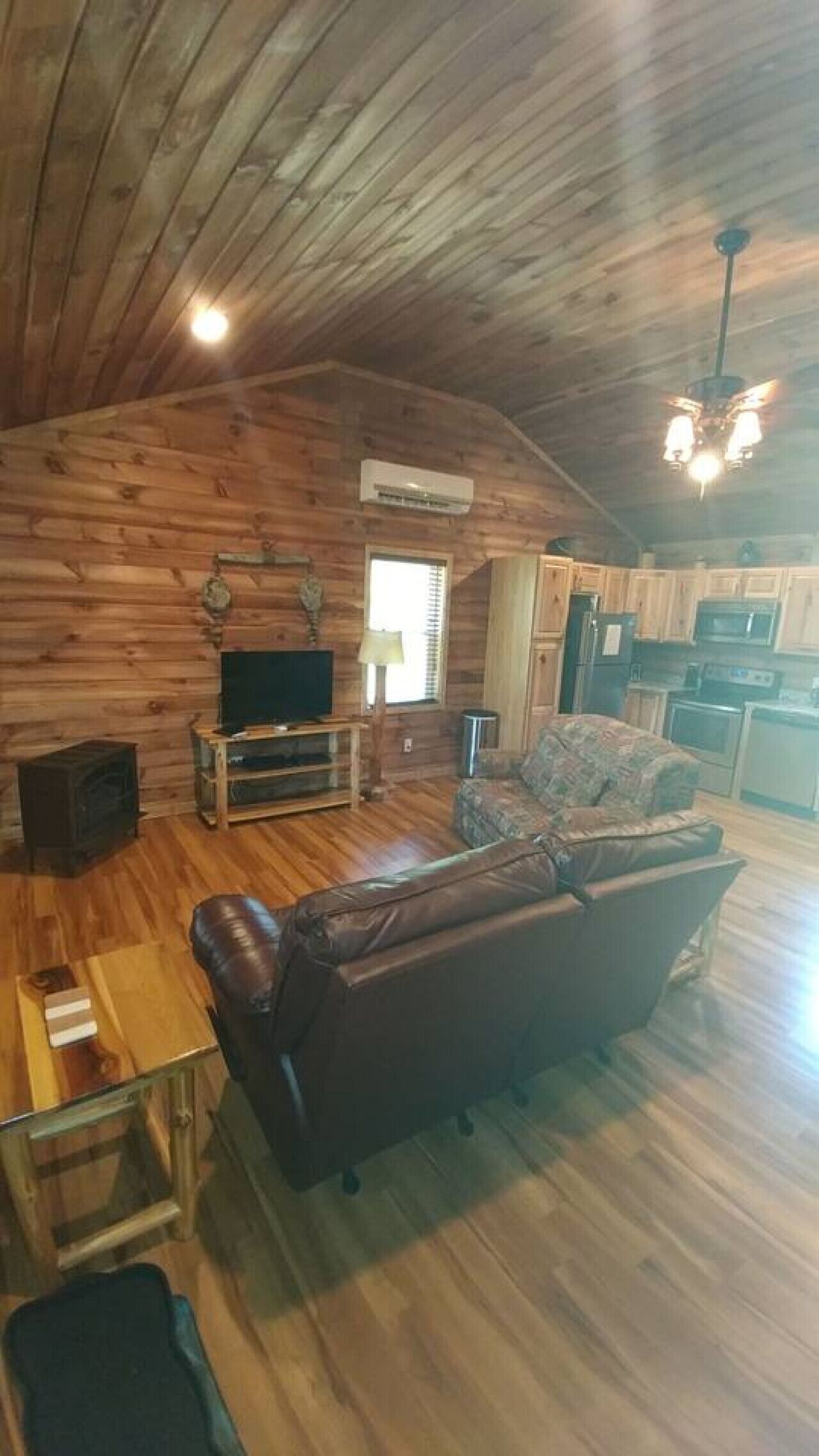 Ein geräumiger Wohnbereich mit Holzboden, Kamin, einer Couch, einem Fernseher und einer Küche im Hintergrund.
