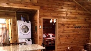 A log cabin interior with a kitchen area featuring wooden cabinets, a granite countertop, and a washing machine. - This cabin is recently constructed and finished November 2016. (Banner Elk)