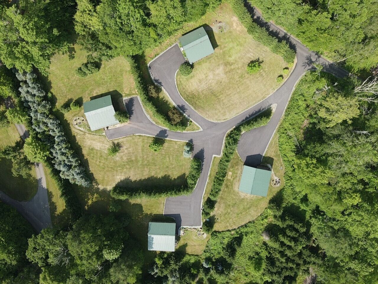 Luchtbeeld van een landgoed met vier gebouwen, een slingerende weg en omliggend groen.