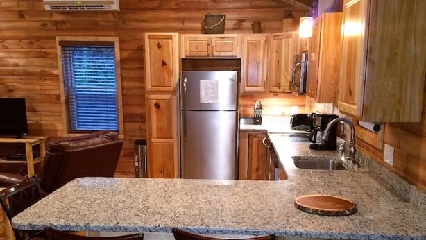 A kitchen with wooden walls, a granite countertop, a stainless steel refrigerator, and bar stools. - This cabin is recently constructed and finished November 2016. (Banner Elk)