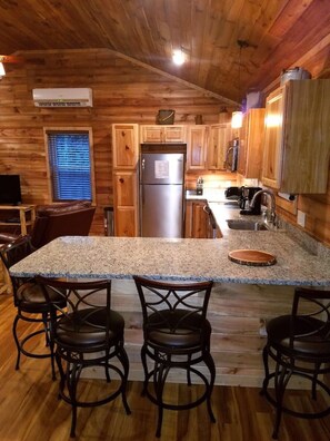 A kitchen with wooden walls, a granite countertop, a stainless steel refrigerator, and bar stools. - This cabin is recently constructed and finished November 2016. (Banner Elk)