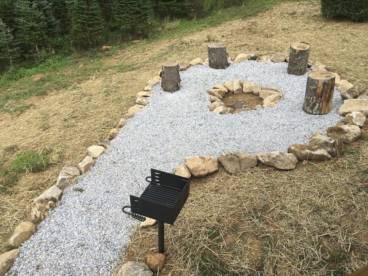 A barbecue grill set up on a gravel path surrounded by rocks and trees.