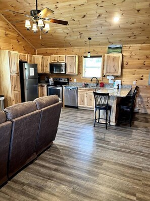 Eine gemütliche Küchenzeile im Chalet-Stil mit Holzausstattung, darunter Kühlschrank, Herd, Mikrowelle und ein Essbereich mit einem Barhocker.