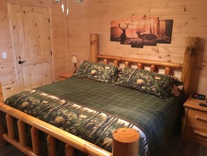 Una habitación de madera con una cama que tiene ropa de cama con estampado de camuflaje, un cabecero de madera y una mesita de noche con un reloj.
