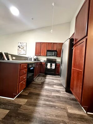 A kitchen with wooden cabinets, a stainless steel refrigerator, a microwave, and a stove.